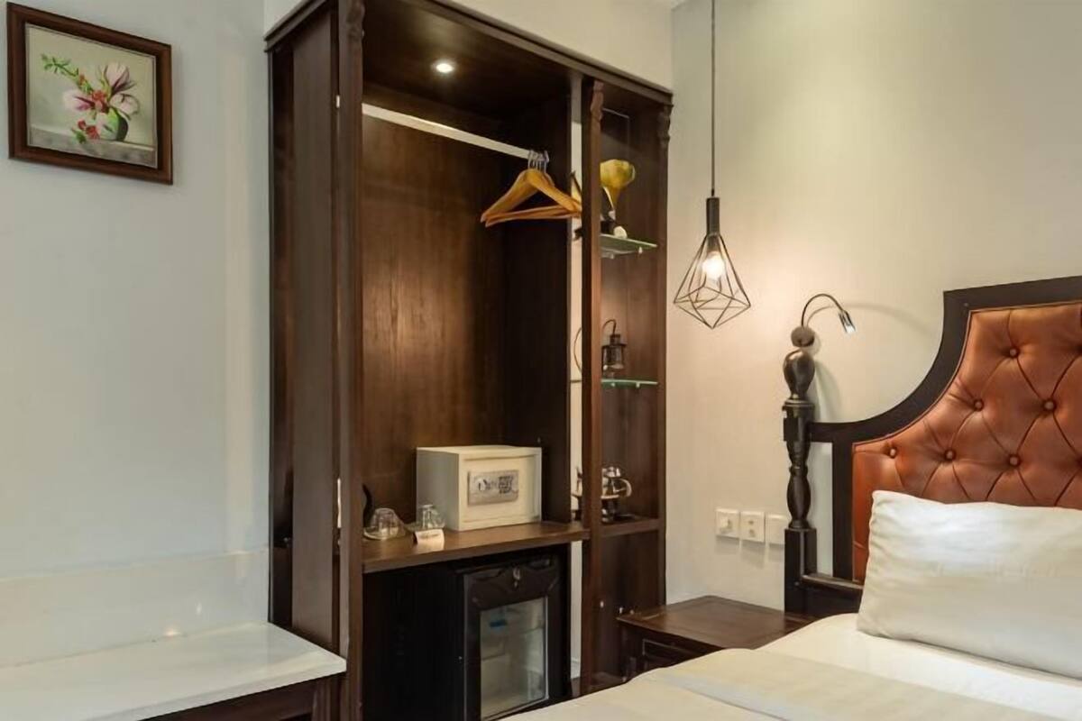 A bedroom with a bed, a wardrobe, a bedside table, a lamp, and a wall-mounted picture.