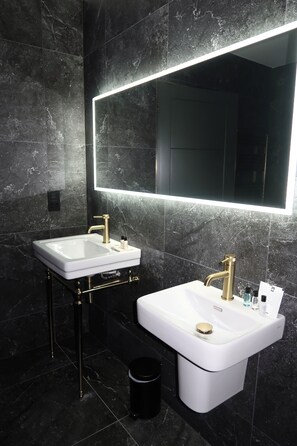 A modern bathroom with two sinks, a large mirror, and a black trash bin.