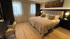 A hotel room with a large bed, a desk, and a chair. There are two nightstands with lamps.
