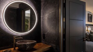 A modern bathroom with a round mirror, a wooden vanity, and a dark marble wall. - House 15 (Kenmare)