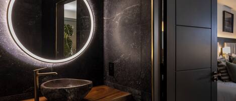 A modern bathroom with a round mirror, a wooden vanity, and a dark marble wall.