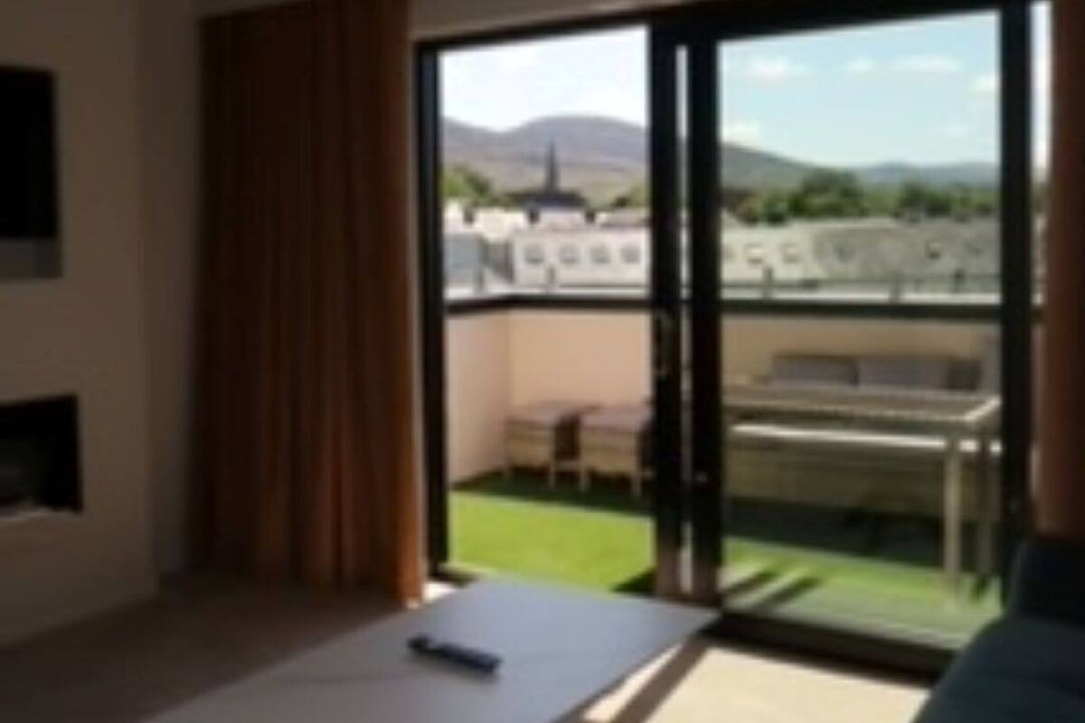 Ein modernes Wohnzimmer mit einer Couch, einem Couchtisch und Blick auf einen Balkon mit Gartenmöbeln.