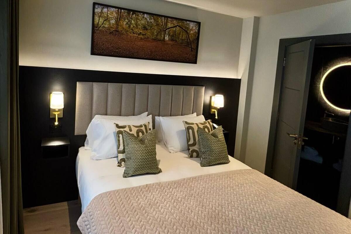 Ein Hotelzimmer mit einem großen Bett, zwei Nachttischen mit Lampen, einem Kopfteil, einem gerahmten Bild über dem Bett und einer Tür mit runder Beleuchtung.