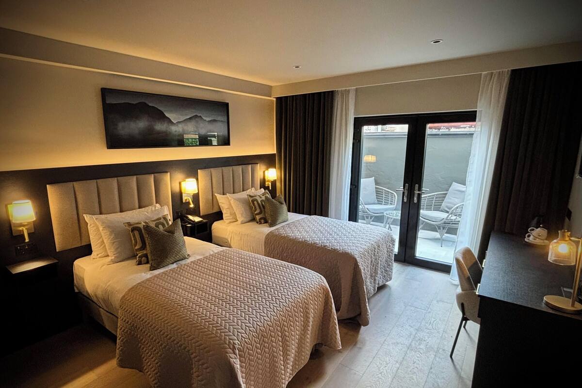 Ein Hotelzimmer mit zwei Betten, einem Schreibtisch und einem Balkon mit Sitzgelegenheit.