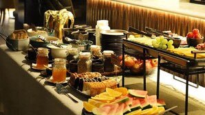 A buffet table with various food items and condiments, a bar area with glasses and bottles, and a brick wall with a patterned design in the background. - House 15 (Kenmare)