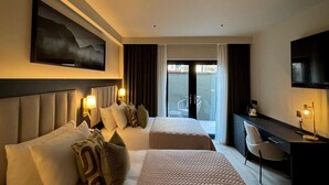 A hotel room with two beds, a desk, a TV, and a large window with a view of the outside. - House 15 (Kenmare)