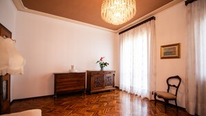 A room with a wooden herringbone floor, a wooden cabinet, a chair, a table with a vase of flowers, a chandelier, and a painting on the wall. - LA VILLETTA DEL NONNO BORTOLO (Castello)