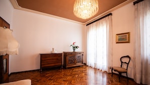 A room with a wooden herringbone floor, a wooden cabinet, a chair, a table with a vase of flowers, a chandelier, and a painting on the wall. - La Villetta del Nonno Bortolo (Castello)
