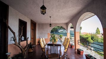 Um alpendre coberto com mesa e cadeiras, plantas em vasos e vista da região ao redor.