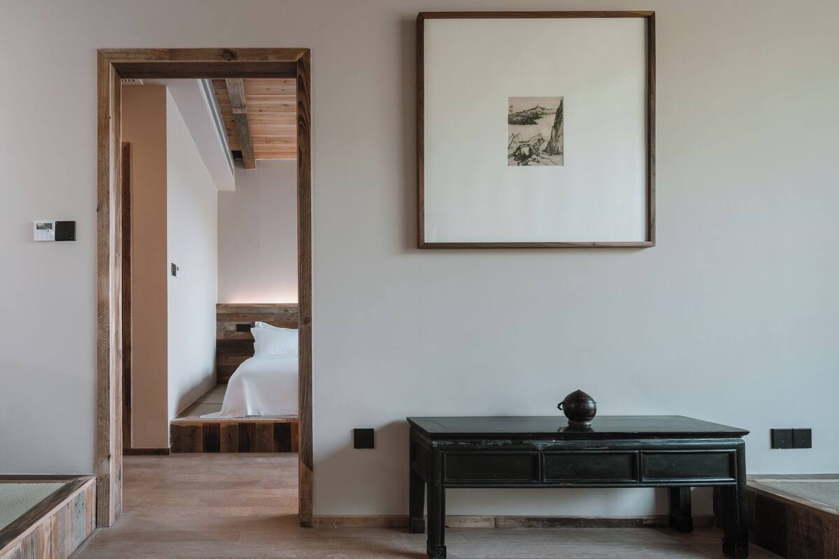 Une chambre d’hôtel avec une tête de lit en bois, un lit, un bureau avec des tiroirs et un tableau encadré au mur.
