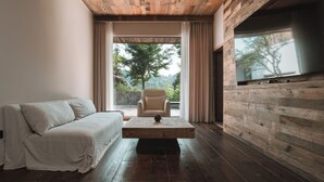 Una sala de estar moderna con techo de madera, un sofá, una mesita de centro y un amplio ventanal con vistas a árboles.