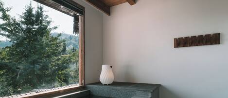 Un baño moderno con encimera de piedra, una toalla blanca y vistas a un bosque a través de un ventanal amplio.