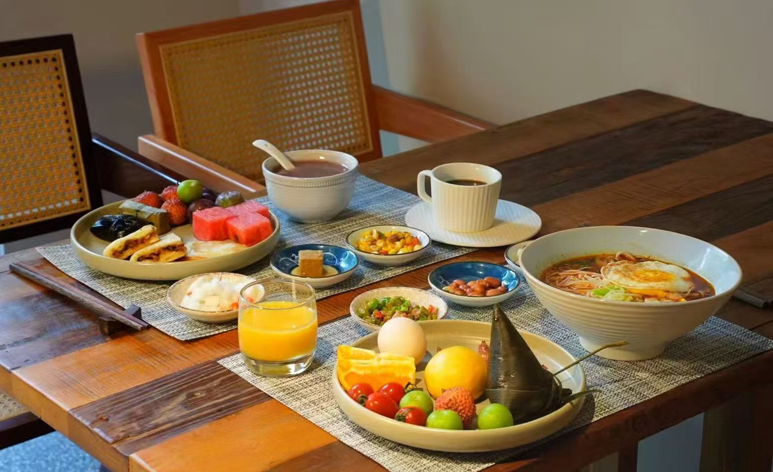 A breakfast table with various dishes including a bowl of soup, a plate of fruit, and a glass of orange juice.