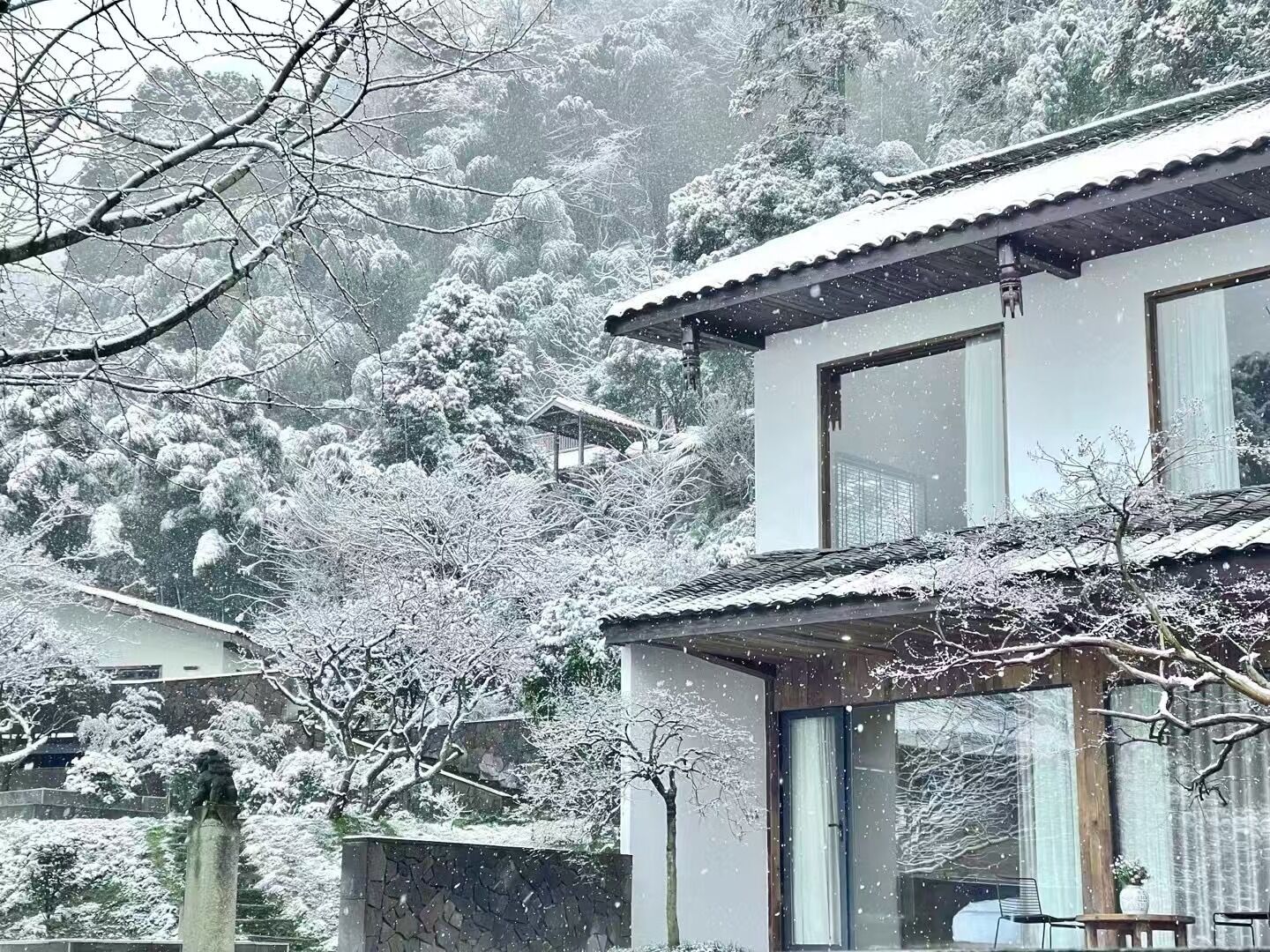 A traditional Japanese-style building with a tiled roof and large windows, surrounded by snow-covered trees and a stone wall.