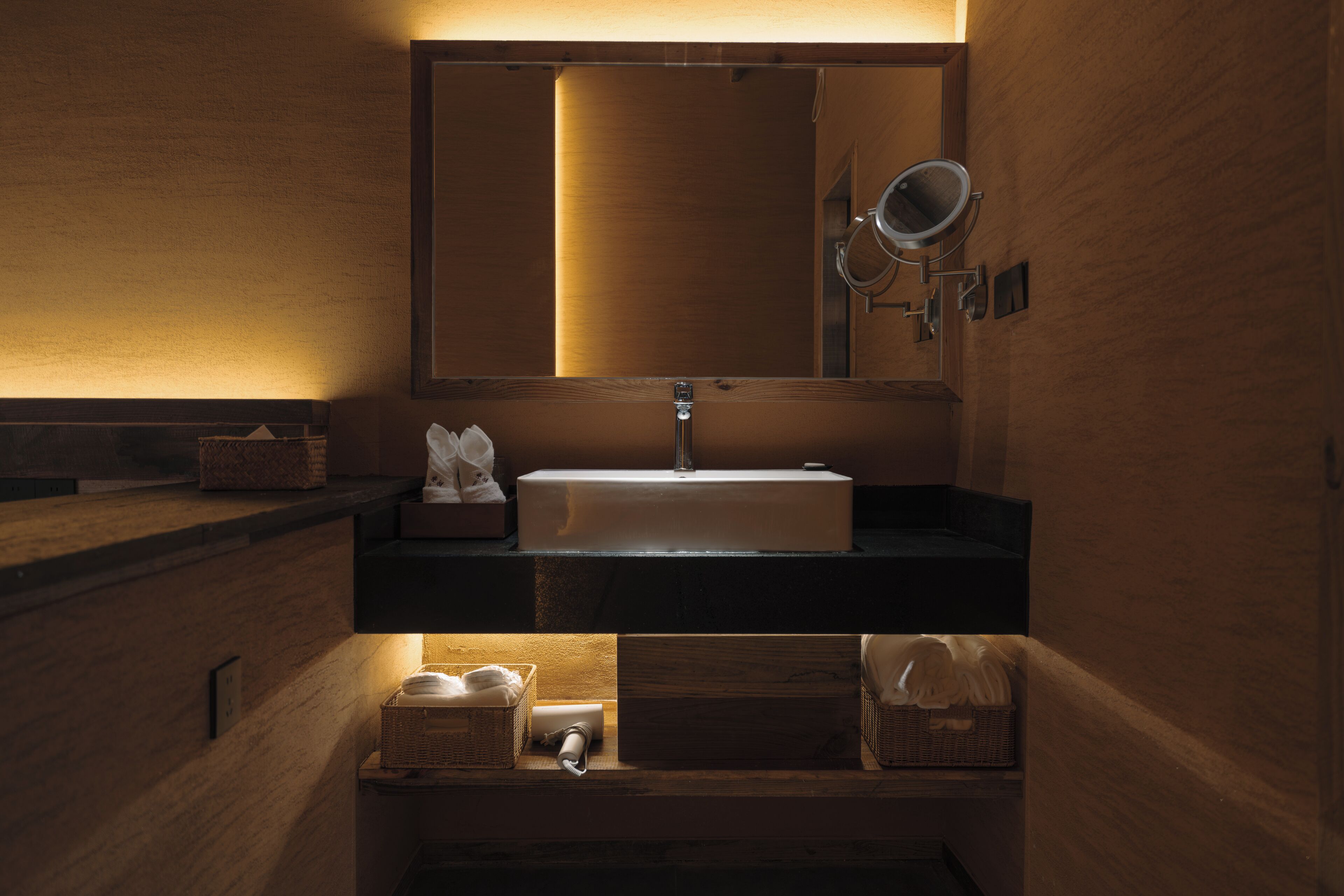 Un baño con tocador de madera, lavamanos, espejo y toallero.