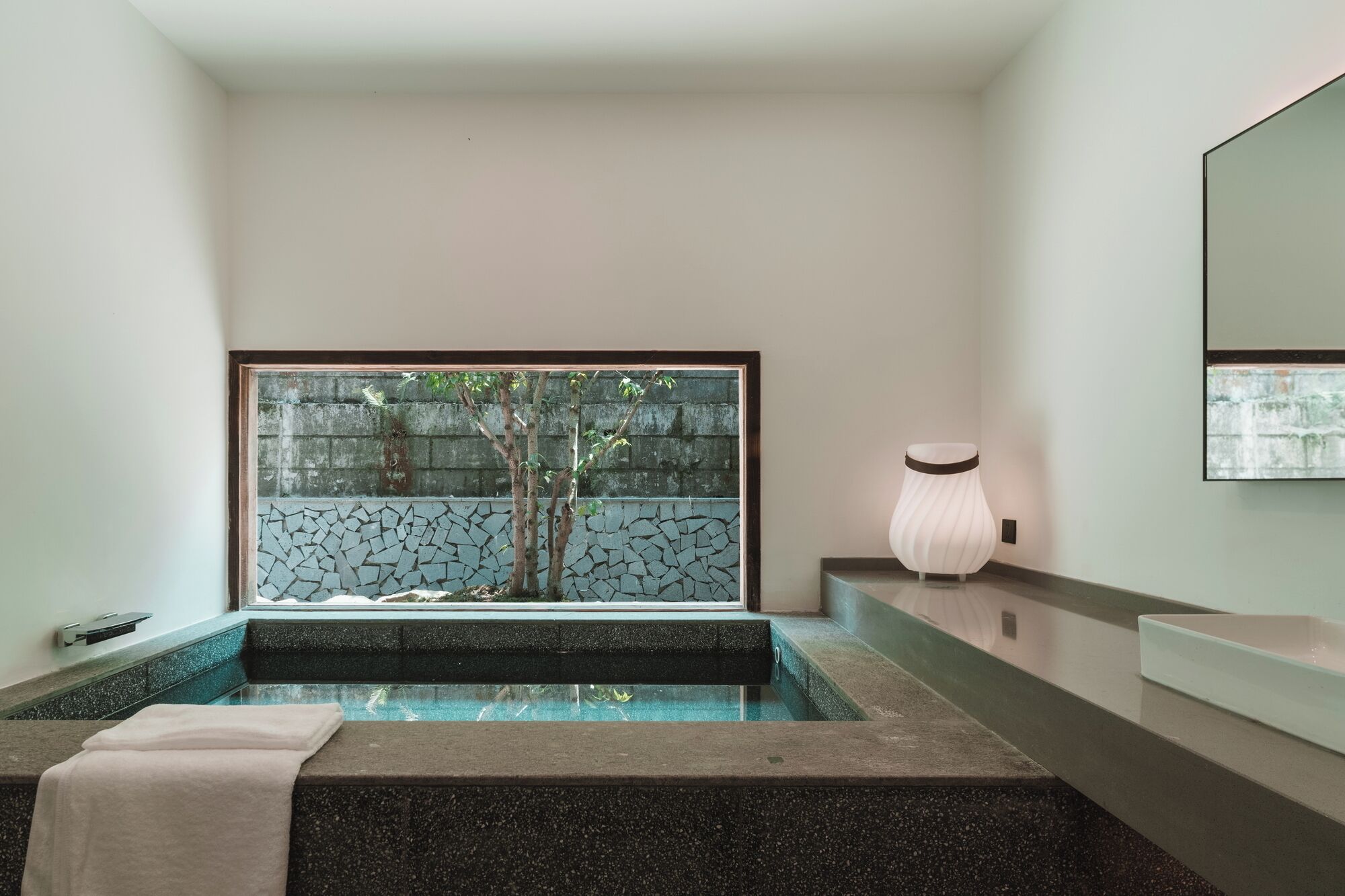 A modern bathroom with a glass-enclosed pool, a stone wall, and a minimalist design.