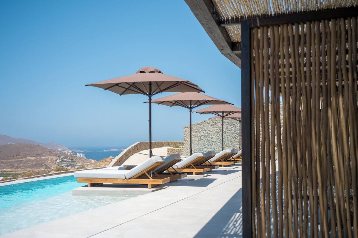 A poolside area with lounge chairs and umbrellas, overlooking a mountainous landscape.
