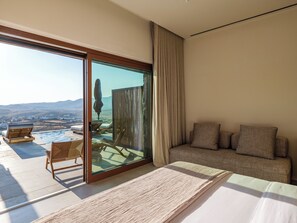 A modern bedroom with a large sliding glass door leading to a balcony with a view of the countryside. - Petrablu Mykonos (Mykonos)