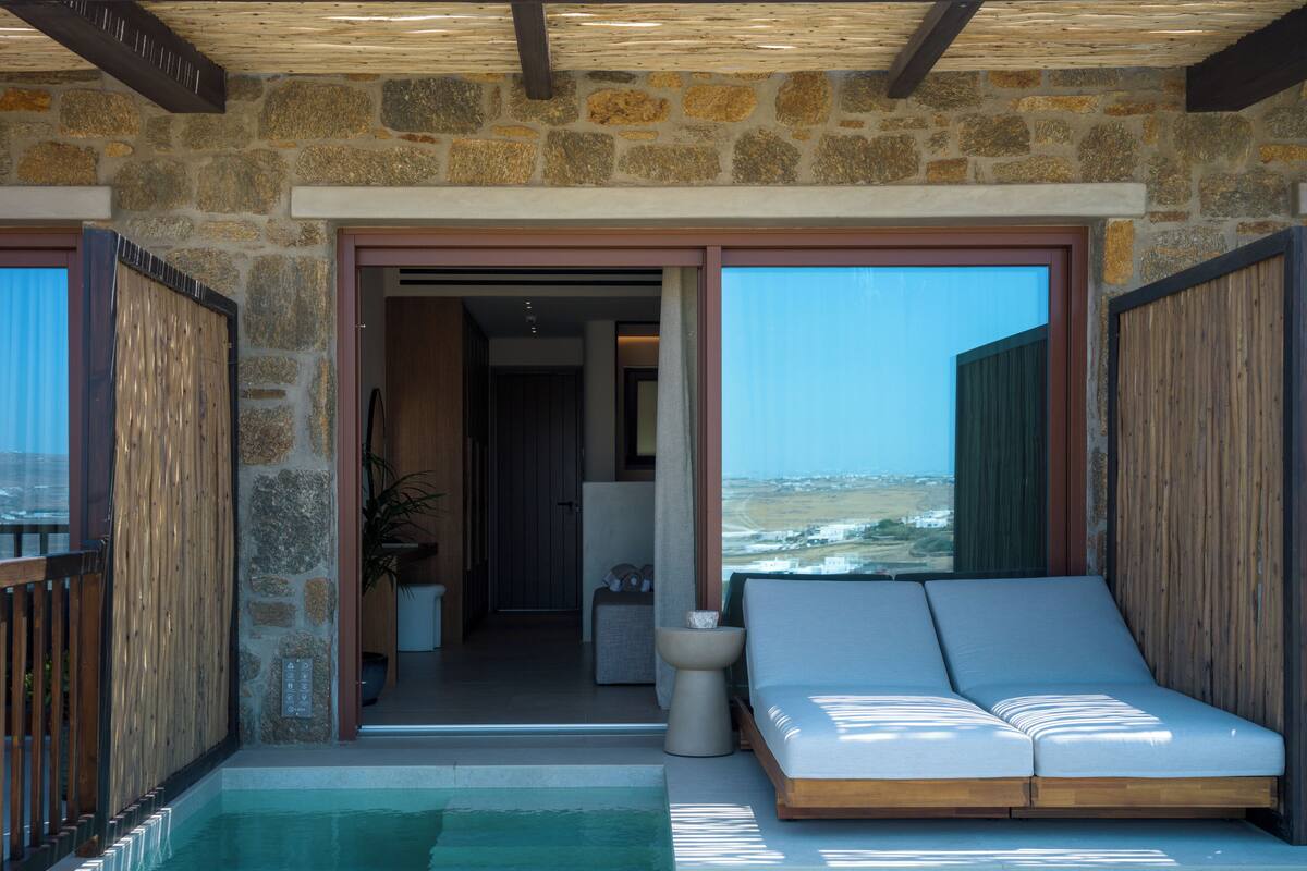 A pool area with a lounge chair, stone walls, and a view of the landscape.