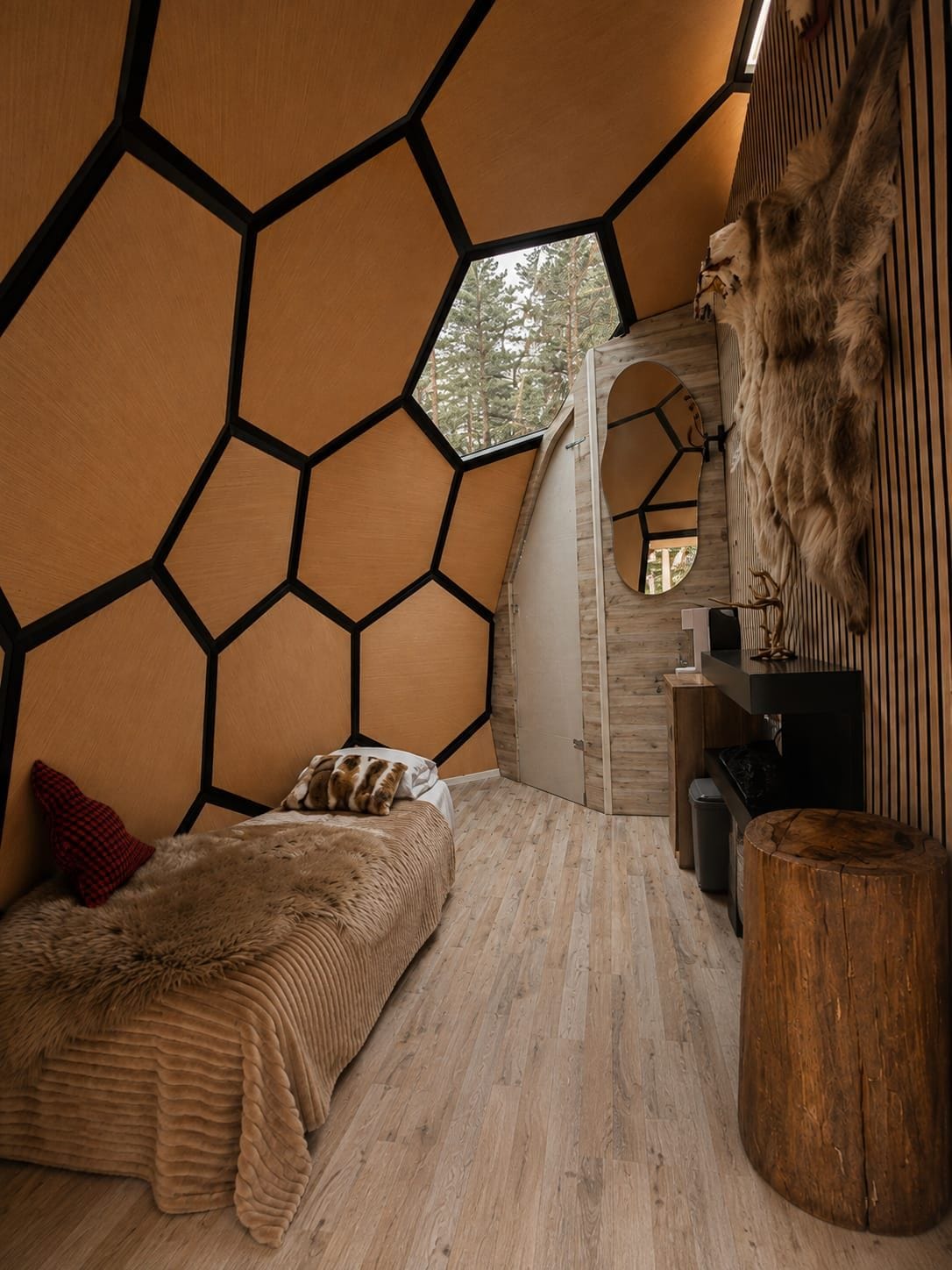 Une pièce dotée d’un plafond à motifs hexagonaux, d’un lit recouvert d’un jeté en fourrure, d’un tabouret en bois et d’un tapis en fourrure.