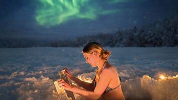 Eine Person sitzt in einer verschneiten Landschaft und blickt auf das Polarlicht.