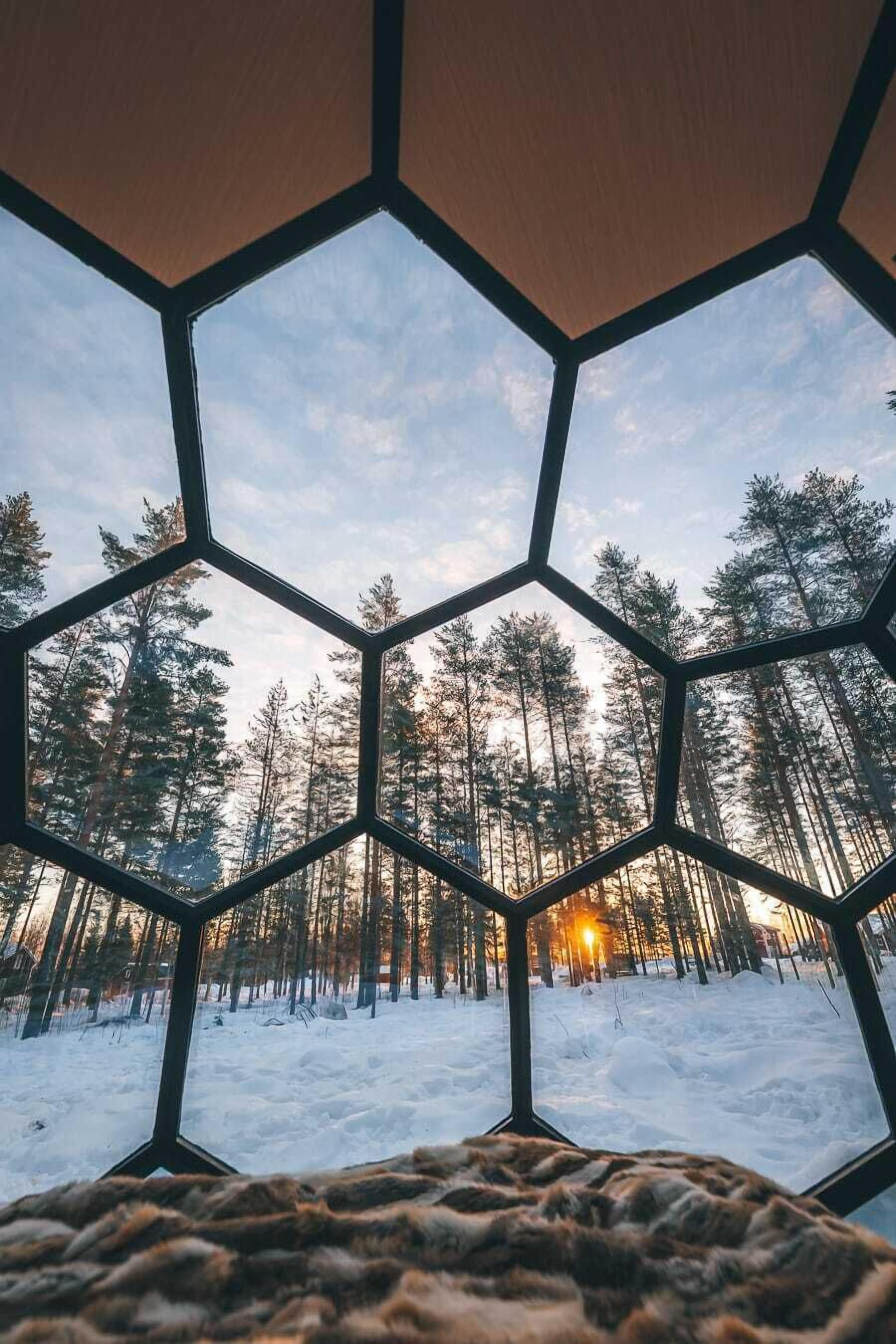 A room with a hexagonal window view of a snowy forest at sunset.