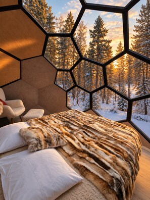 Ein Schlafzimmer mit einem großen Fenster, das einen verschneiten Wald zeigt.