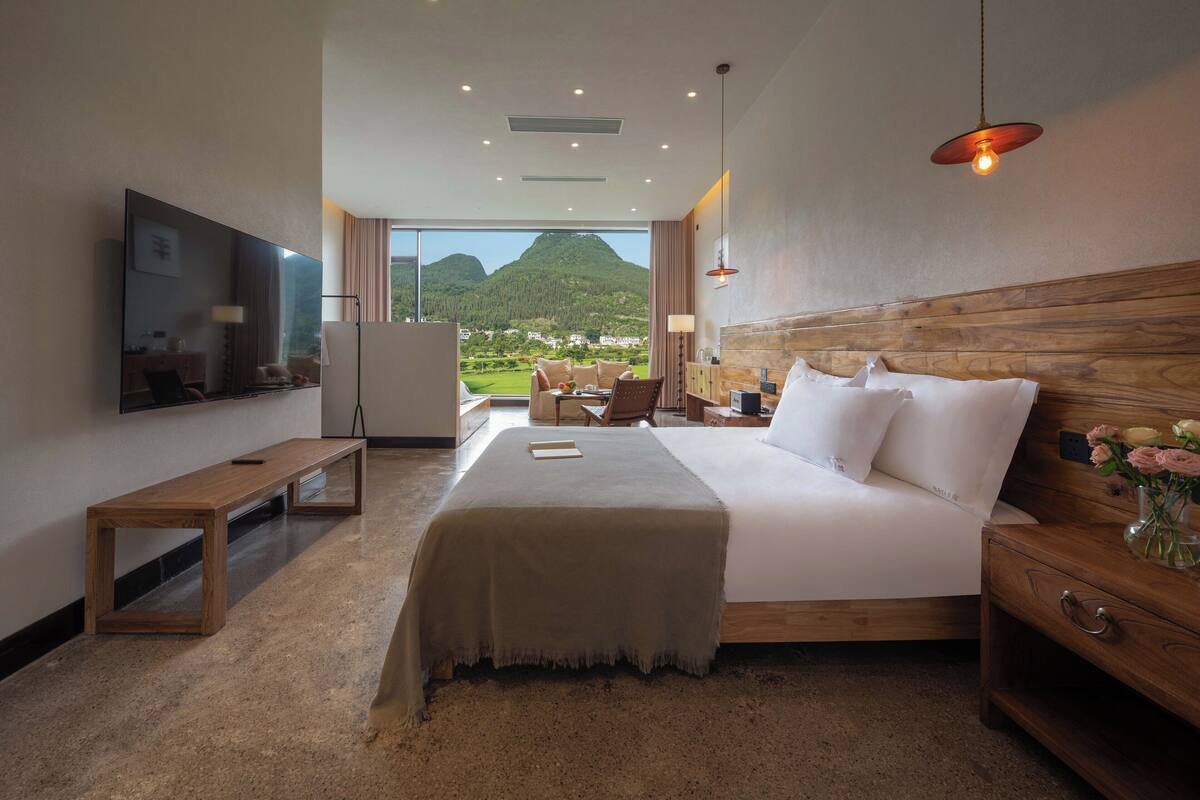 Ein Hotelzimmer mit einem großen Bett, einem Fernseher, einem Schreibtisch und Blick auf die Berge.