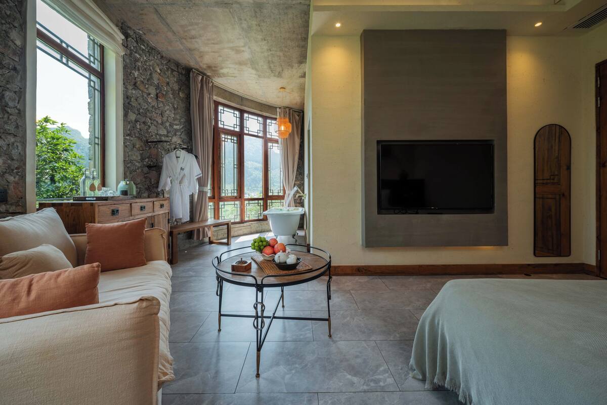 Ein geräumiges Zimmer mit einem großen Bett, einem Sofa, einem runden Couchtisch und einem an der Wand befestigten Fernseher.
