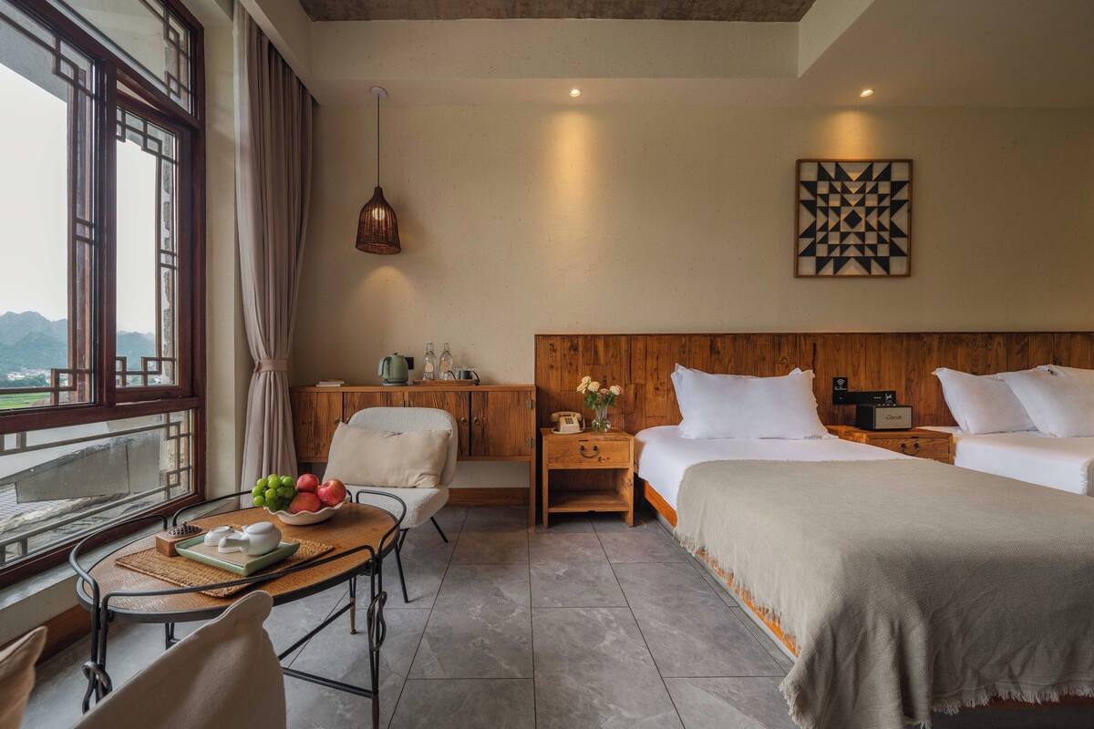 Ein Hotelzimmer mit Bett, Nachttisch, Sessel und Blick auf Berge durch ein Fenster.