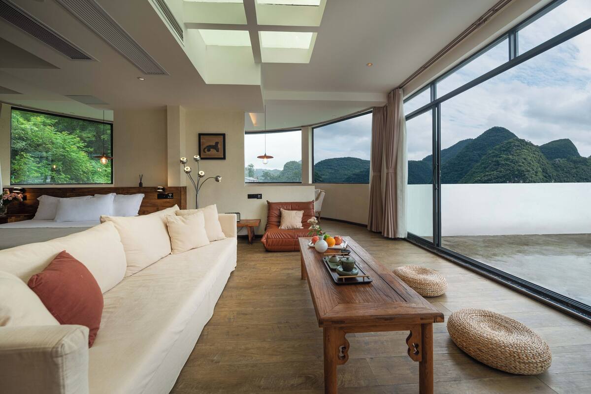 Ein modernes Wohnzimmer mit einer Couch, einem Holztisch und Blick auf Berge durch große Fenster.