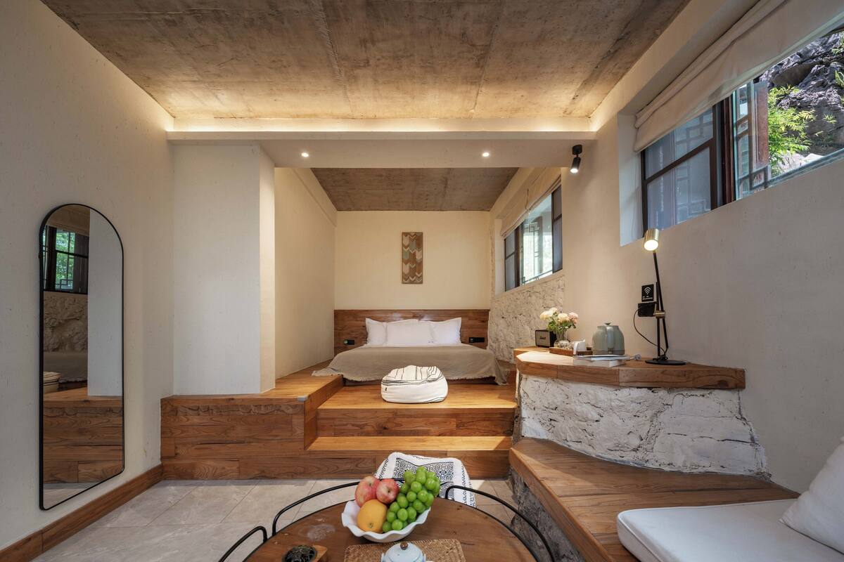Ein modernes Schlafzimmer mit einem Holzkopfstück, einem Nachttisch mit Lampe und einer Obstschale auf dem Boden.