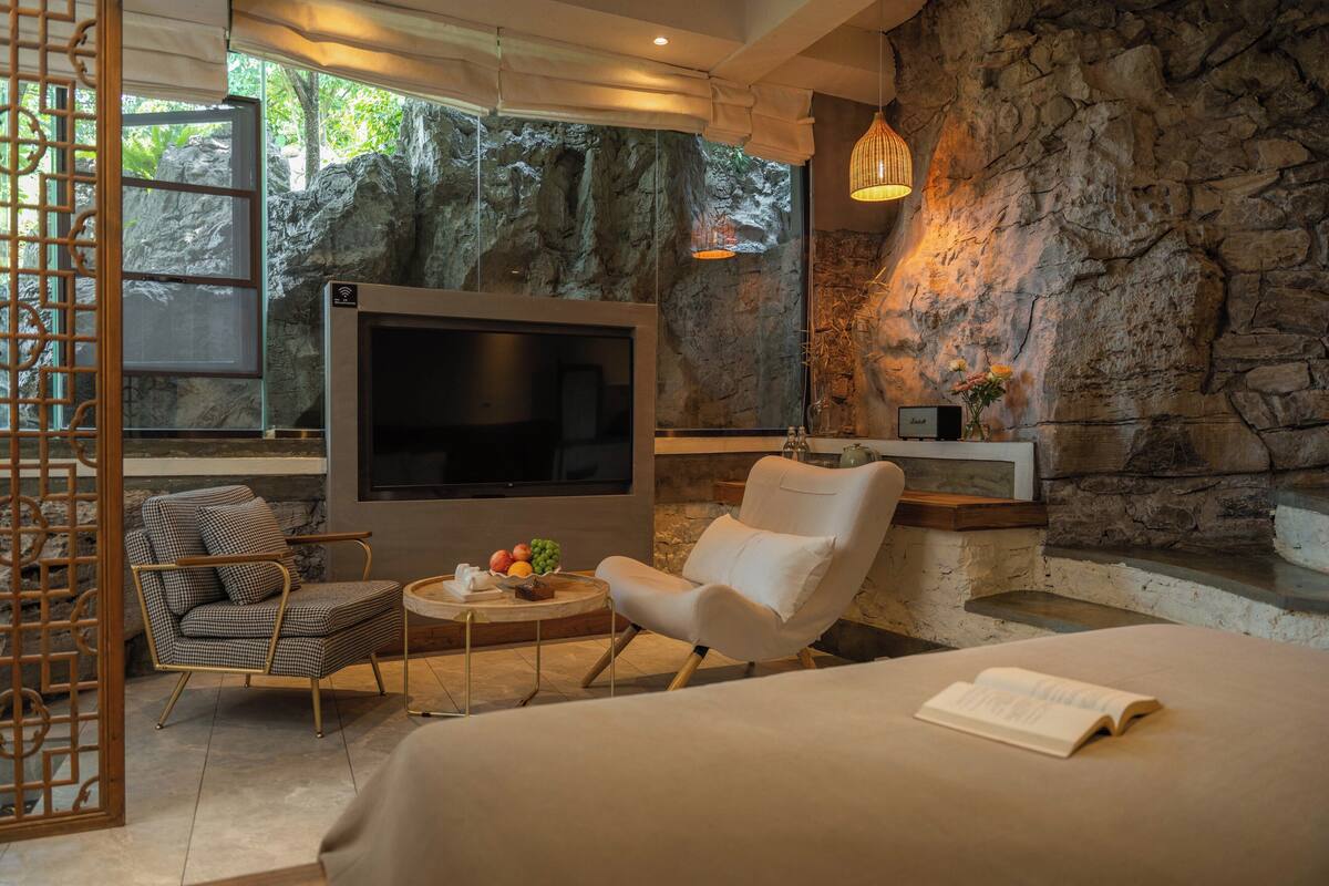 Ein modernes Schlafzimmer mit einem großen Bett, einem Fernseher, einer Steinwand und Blick auf eine felsige Landschaft.