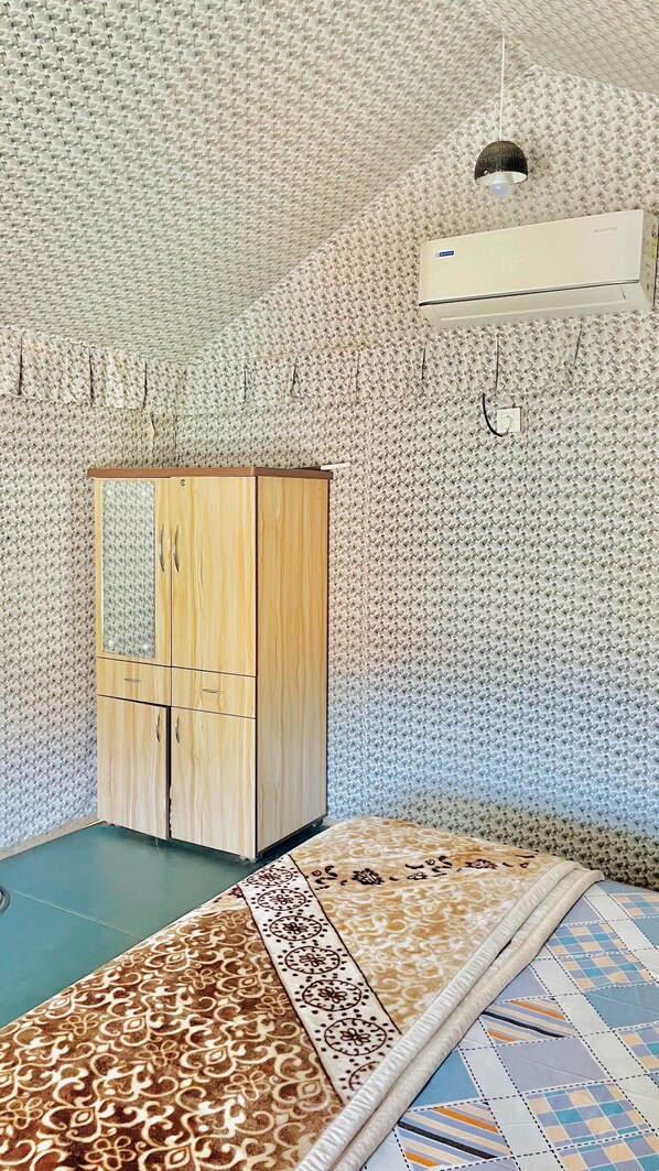 Una habitación con pared estampada, un armario de madera, una cama con ropa de cama estampada y un aire acondicionado.