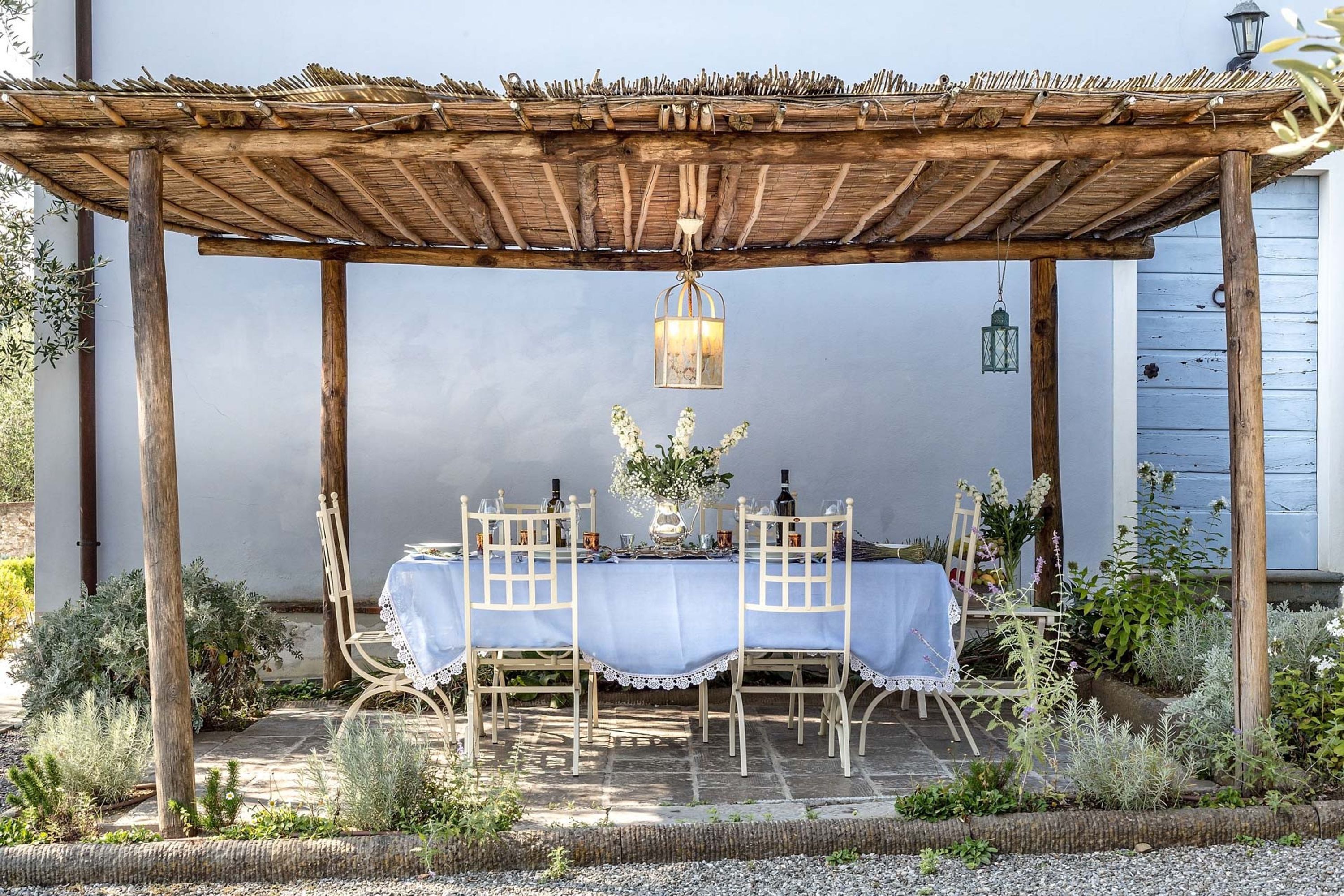 Un espace extérieur aménagé, abrité et doté d’une table pour deux, entouré de plantes et surmonté d’une pergola.