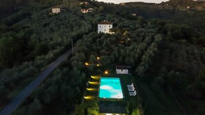 Une vue aérienne d’une propriété dotée d’une piscine entourée de verdure, avec une route et quelques bâtiments en arrière-plan.