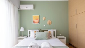 A neatly made bed with white linens, two bedside tables with lamps, a wall-mounted air conditioner, and a large wardrobe. - Santorini-2-Bedroom Apt in Nea Smyrni (Nea Smirni)