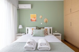 A neatly made bed with white linens, two bedside tables with lamps, a wall-mounted air conditioner, and a large wardrobe.