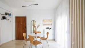 A dining area with a round table, four wicker chairs, a mirror, and a bookshelf with books. - Santorini-2-Bedroom Apt in Nea Smyrni (Nea Smirni)