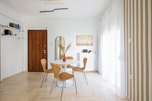 A dining area with a round table, four wicker chairs, a mirror, and a bookshelf with books.