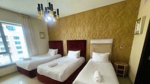 A hotel room with three beds, a small wooden stool, and a window with curtains.