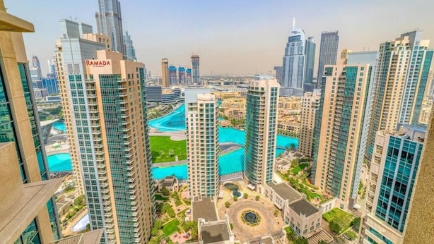 A high-rise building with a prominent "RAMADA" sign, surrounded by other tall buildings and a central water feature.