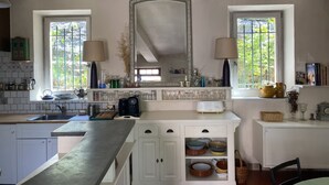 A kitchen with white cabinets, a large mirror, and two windows with curtains. - La Maison Rose, family vacation home (Lagnes)