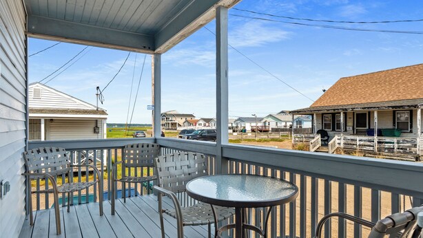 A covered outdoor area with a table and chairs, a view of neighboring houses, and a clear sky. - Charming 2-Bedroom Getaway A/C, WIFI, Covered porch just 3 Minutes to the Beach! (Hampton)