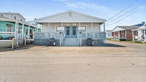 A two-story building with a central entrance, a covered porch, and a gravel driveway. - Charming 2-Bedroom Getaway A/C, WIFI, Covered porch just 3 Minutes to the Beach! (Hampton)