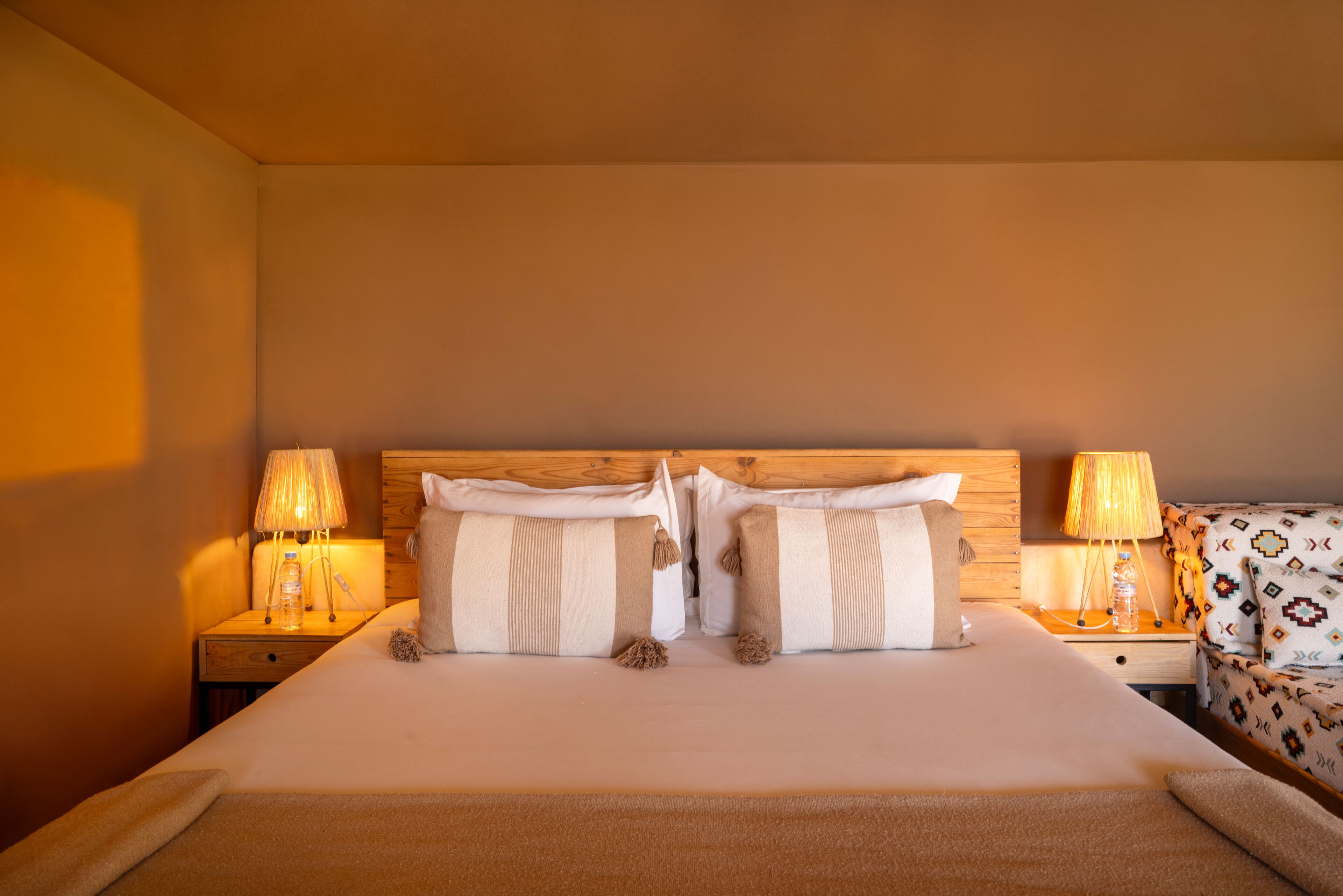 Una habitación de hotel con una cama, dos lámparas de noche, un cabecero de madera y un sillón con estampado.