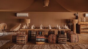 A dining area with a long wooden table set for a meal, surrounded by striped ottomans and a woven chair. - Mia Agafay Resort (Agafay)