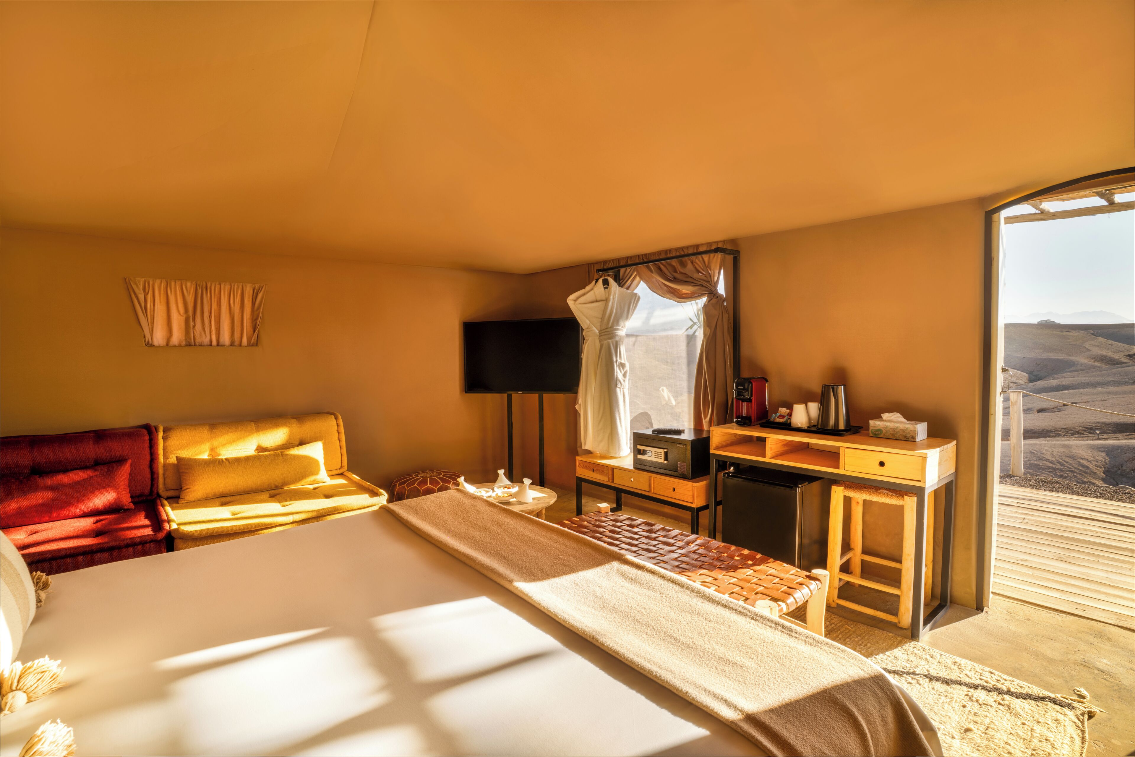 A hotel room with a bed, a desk, a mirror, a TV, and a view of the desert.