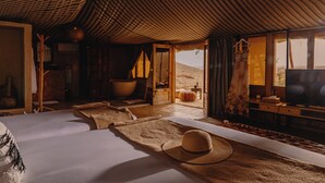 A spacious room with a large bed, a television, and a view of the desert outside. - Mia Agafay Resort (Agafay)
