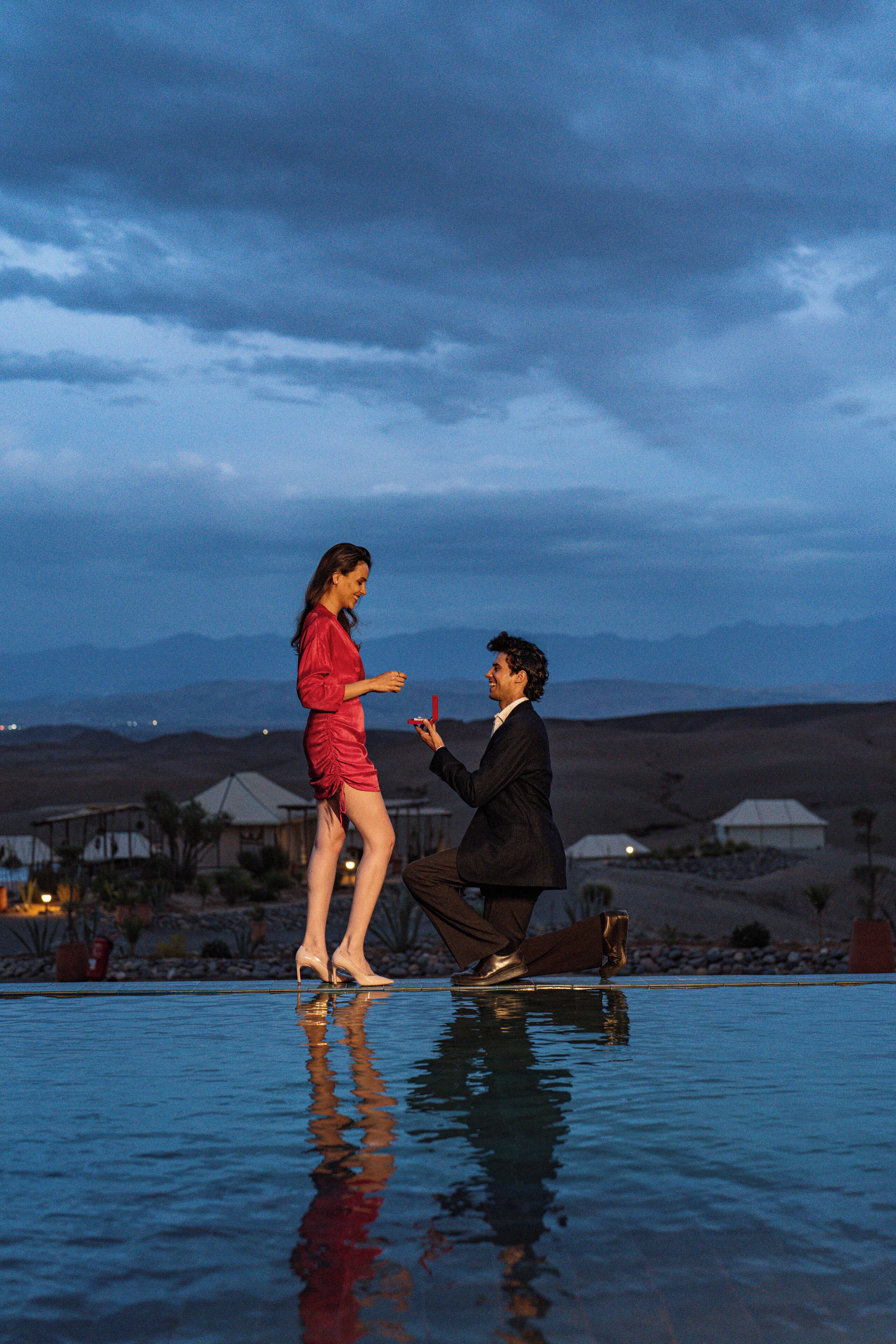 A man proposing to a woman by the poolside at dusk.